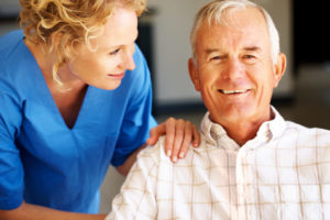 A smiling senior man and a smiling caregiver with her hand on his shoulder.